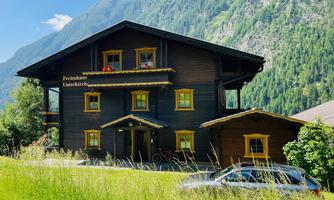 A charming black wooden house in the mountains with colorful window frames. Surrounded by green meadows and mountains in the background.