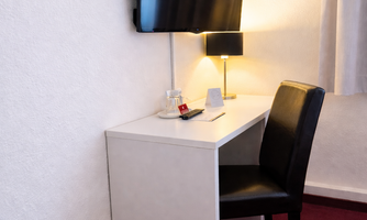 A simple room with a desk, a television, and a chair. Next to the desk, there is a small lamp on the table.