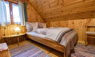 A cozy bedroom with wood paneling and a large bed. The room is bright and friendly, with a small table and a rug.