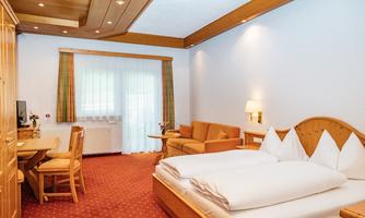 A cozy hotel room with a double bed, a table, and chairs. There is a seating area with a sofa and light wood interior.