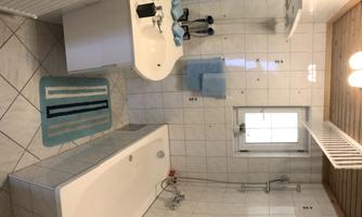 A modern bathroom with a bathtub and a sink. It features bright tiles and is decorated with blue towels.