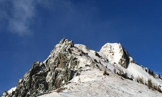 An impressive mountain with snow-covered peaks and a clear blue sky. The rocks are steep and prominent.