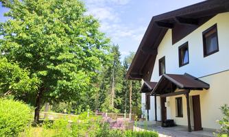 A beautiful house surrounded by trees and colorful plants. The sky is blue and the atmosphere is calm and inviting.