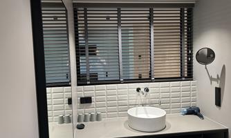A modern bathroom with a round washbasin and a large mirror. Blinds and discreet lighting create a pleasant atmosphere.