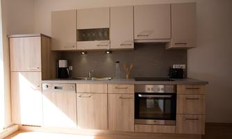 A modern kitchen with wooden fronts and a gray countertop. It is well equipped with a stove, a sink, and kitchen utensils.