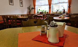 A cozy restaurant with wooden furniture and orange curtains. On the table are spice shakers and a sugar bowl on an orange placemat.