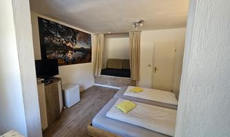 A cozy room view with two beds and a small refrigerator. A landscape picture hangs on the wall and there is a seating area with curtains.