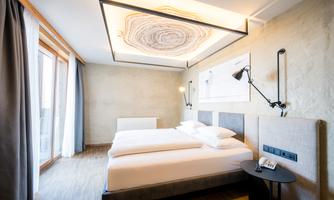 A modern hotel room with two single beds and elegant design. Large windows provide plenty of natural light.