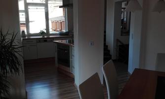 A bright kitchen with modern appliances and a dining area. In the background, stairs and plants are visible.