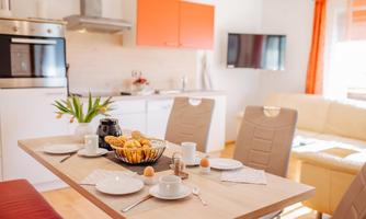 A modern kitchen with a dining table set with breakfast offerings. Bright colors and an inviting atmosphere characterize the space.