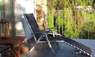 A cozy lounge chair on a terrace overlooking green trees. The place radiates tranquility and relaxation.