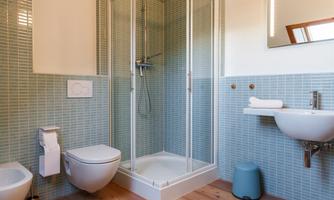A modern bathroom with a shower, a sink, and a toilet. The walls are tiled in soft shades of blue, and the wooden floor provides a warm contrast.