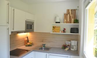 A modern kitchen with white furniture and a wooden shelf. Fresh ingredients and kitchen appliances are on the countertop.