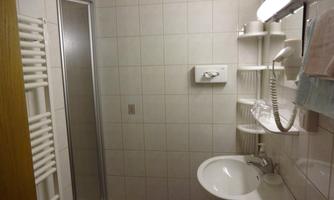 A small bathroom with a shower and sink. The walls are tiled and there are shelves for toiletries.