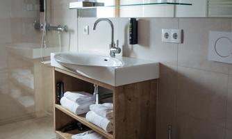 A modern bathroom with a shower, a sink, and a toilet. Towels are neatly stacked on a wooden shelf.