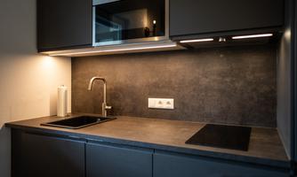 A modern kitchen with dark furniture and an elegant countertop. It is equipped with a sink, a stove, and a microwave.