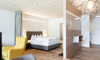 A modern room with a large bed and a cozy armchair. The room is bright and designed in a minimalist style.