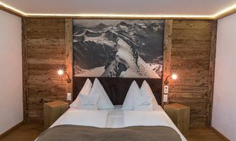 A cozy bedroom with a double bed and modern wood details. The wall art features an impressive mountain landscape.
