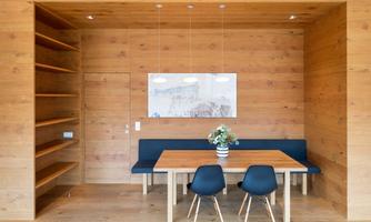 A modern dining area with wooden walls and a large table. There are two chairs and a flower in a vase on the table.