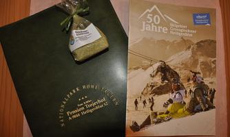 A green brochure and a small gift that is in transparent packaging. Next to it lies a brochure titled "50 Years".