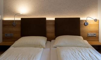 A cozy bedroom with two beds and warm wall lighting. The decor is modern and simple.