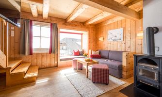 A cozy wooden house with a bright living room. There is a sofa, a table, and large windows that provide a view outside.