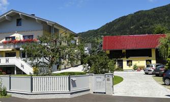 A beautiful residential building with a modern appearance and many windows. In the foreground, there is a well-kept garden and a driveway to another house.