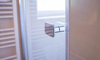 A modern shower room with a glass shower door. The stainless steel door handle is clearly visible.