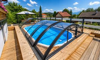 A beautiful swimming pool with a transparent cover in a light-filled environment. The terrace is made of wood and offers a great view of the landscape.