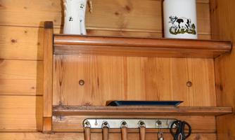 A rustic wooden kitchen shelf with cooking utensils and a vase of dried flowers. Below it are various kitchen tools on a hook rack.