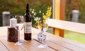 A cozy table with a bottle of wine, two glasses, and a candle. Colorful flowers in a small vase complete the arrangement.