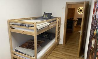 A simple bedroom with a wooden bunk bed. In the background, an open door to another room is visible.