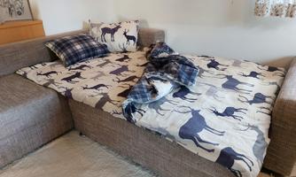 A cozy sofa with a bed sheet in animal print, which is partially wrinkled. There are cushions and a blanket that lie messily on the bed.