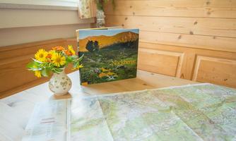 A wooden table with a map and a book about the Nock Mountains.  
On the table, there is a small vase with colorful flowers.