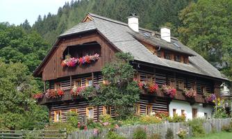 A charming wooden house with colorful flower boxes. Surrounded by a green meadow and tall trees.