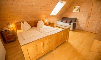 A cozy wooden bedroom with a double bed and two pillows. There is also a seating area with a sofa and natural light through a skylight.