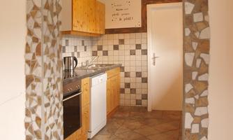 A modern kitchen with wooden cabinets and a tiled floor. The entrance is framed by a decorative arch.