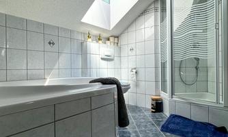 A modern bathroom with a large bathtub and a shower. Bright tiles and daylight create an inviting atmosphere.