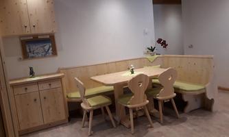 A bright dining room with a wood-paneled seating area and a table. There are five chairs and a small kitchen in the corner.