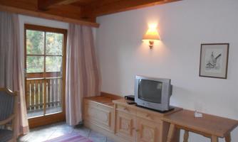 A cozy living space with wood paneling and a television. Bright curtains and a window provide a view outside.