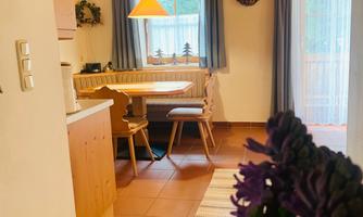 A cozy kitchen with a dining table and wooden decor. In the foreground are purple flowers in a vase.