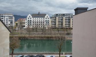 A calm river with modern urban architecture in the background. The clouds create a gloomy atmosphere.