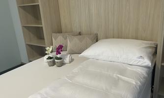 A simple bedroom with a bed, a pillow, and small plants on the table. In the background, wooden shelves are visible.