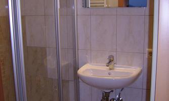 A modern bathroom with a shower and a sink. The walls are light tiled and there is a large mirror.