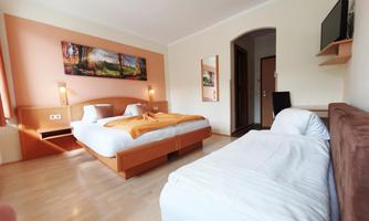 A bright hotel room with a double bed and a single bed. The walls are painted in soft colors, and a flat-screen TV is visible.