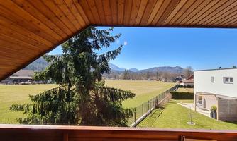 A beautiful view from a balcony of a green meadow and mountains in the background. The sky is clear and blue.