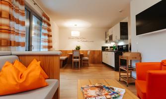 A cozy living space with modern furniture and an open kitchen. Bright colors and natural light sources create an inviting atmosphere.
