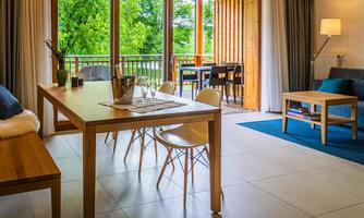 A bright and modern living space with a wooden dining area. The balcony door opens to a green view.