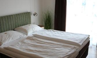 A modern bedroom with a double bed and white bedspreads. Large windows provide plenty of daylight and a pleasant atmosphere.