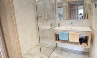 A modern bathroom with a large shower and a bright sink. Colorful towels are laid out on the sink and a soft rug.